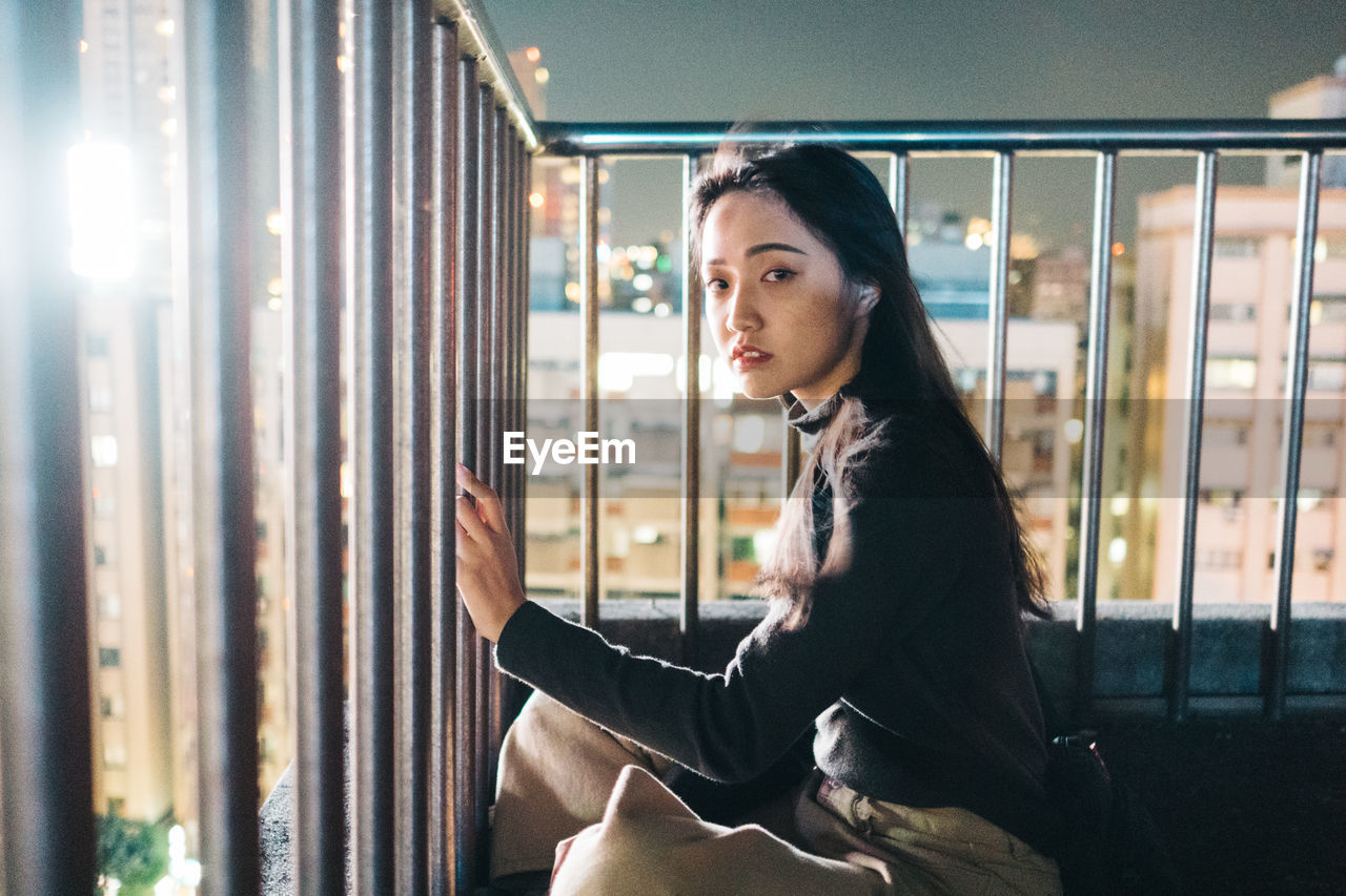 PORTRAIT OF YOUNG WOMAN SITTING IN WINDOW