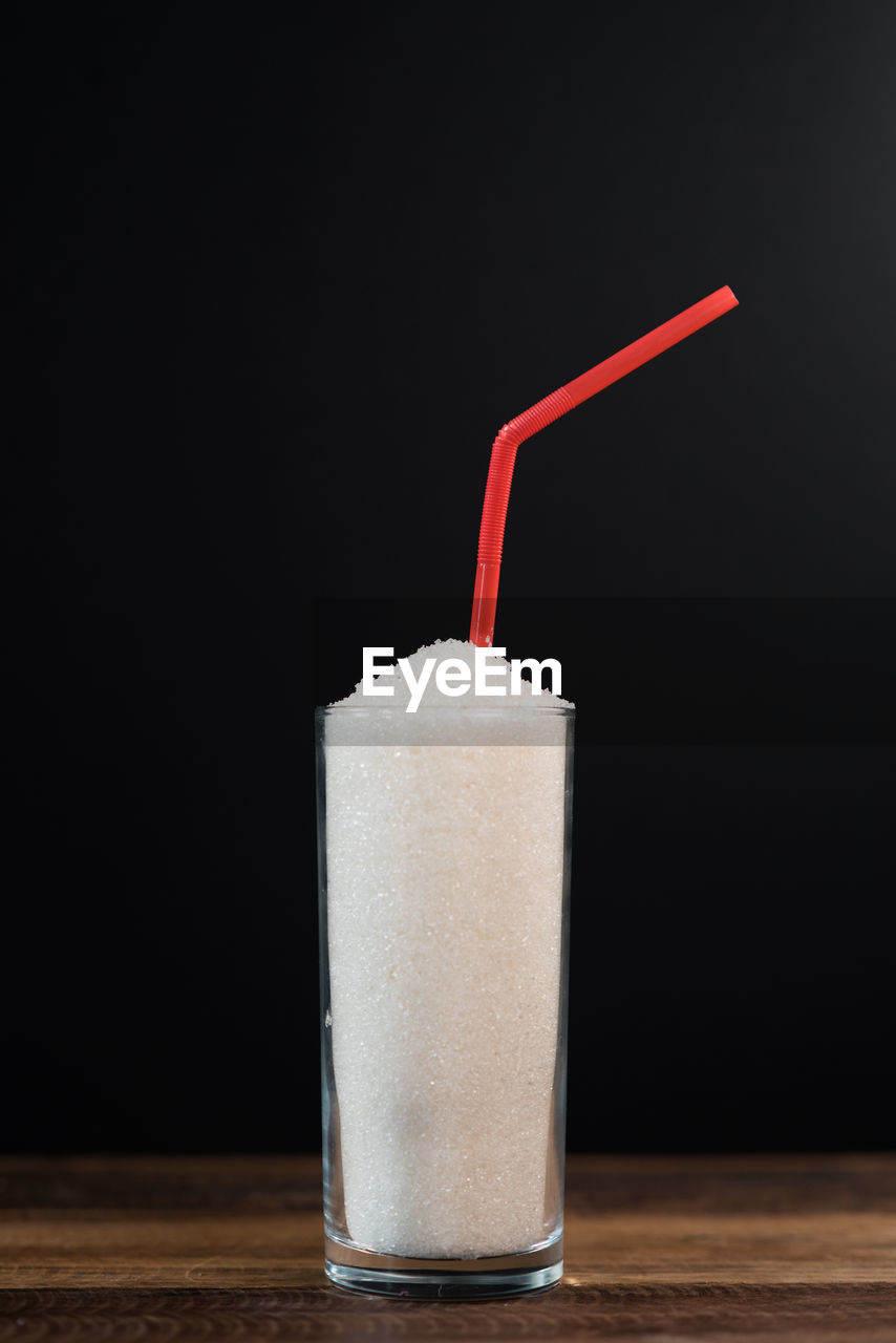 A glass full of sugar with straw against black background. concept of unhealthy eating, diabetes