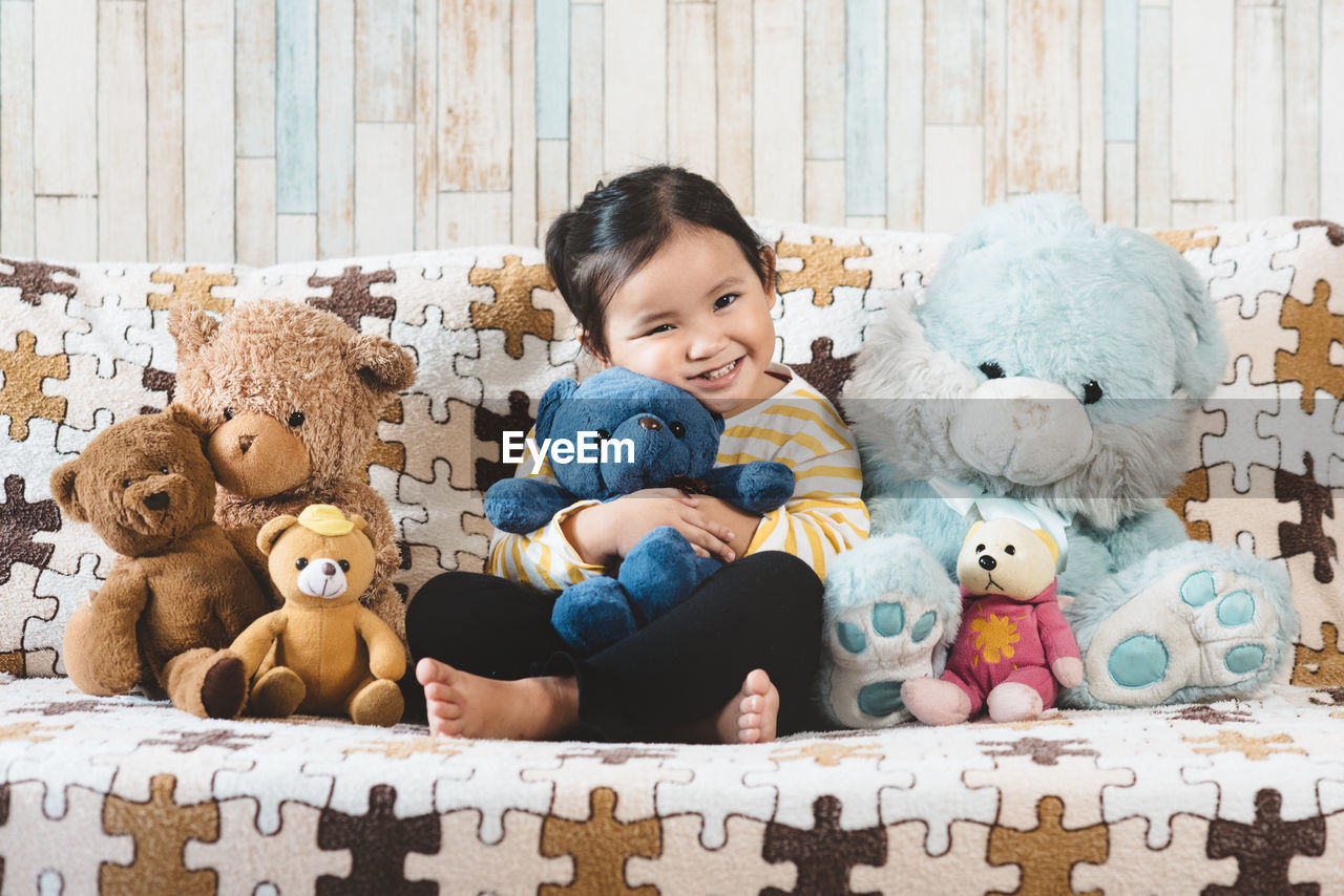 Portrait of girl sitting with teddy bears on sofa at home