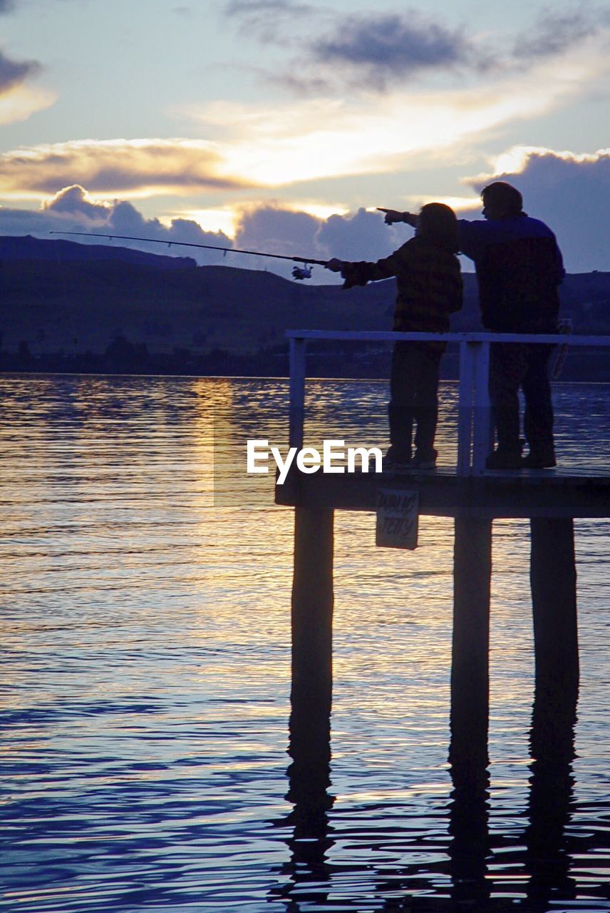 REAR VIEW OF SILHOUETTE MAN STANDING ON LAKE AGAINST SKY