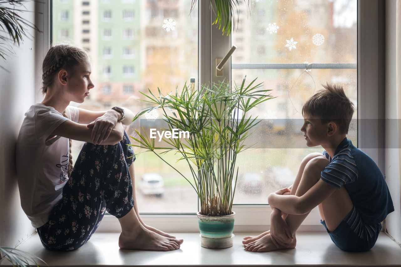 Side view of children sitting against window