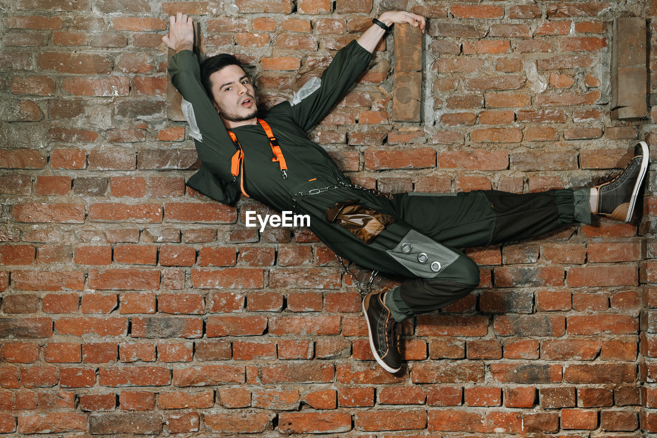 Portrait of man climbing on brick wall