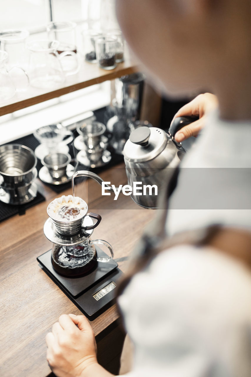 High angle cropped image of barista pouring boiling water in coffee filter at counter