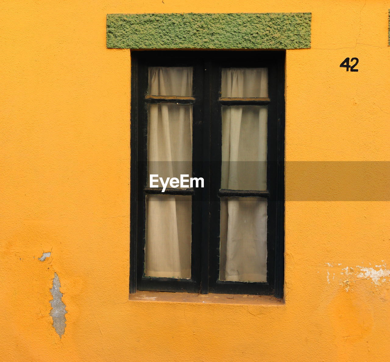 Traditional portuguese window with a green top inserted in a yellow wall