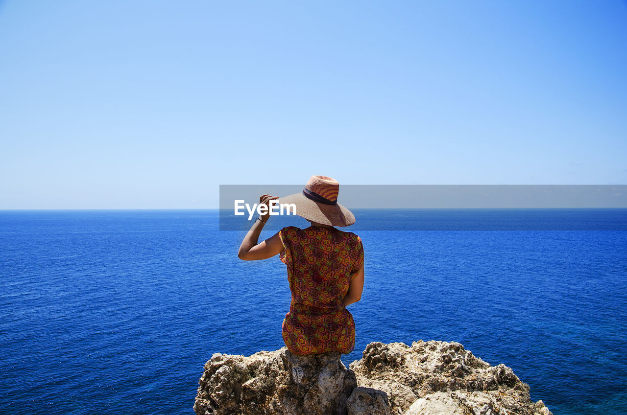Rear view of woman sitting on rock against sea and sky
