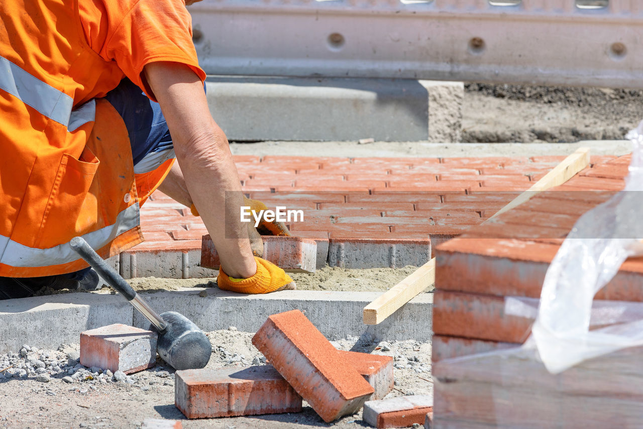 A worker lays orange paving slabs on the sidewalk on a sunny summer day.