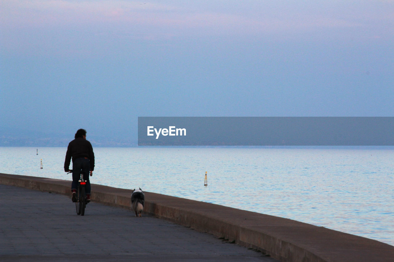 REAR VIEW OF MAN WALKING AT BEACH AGAINST SKY