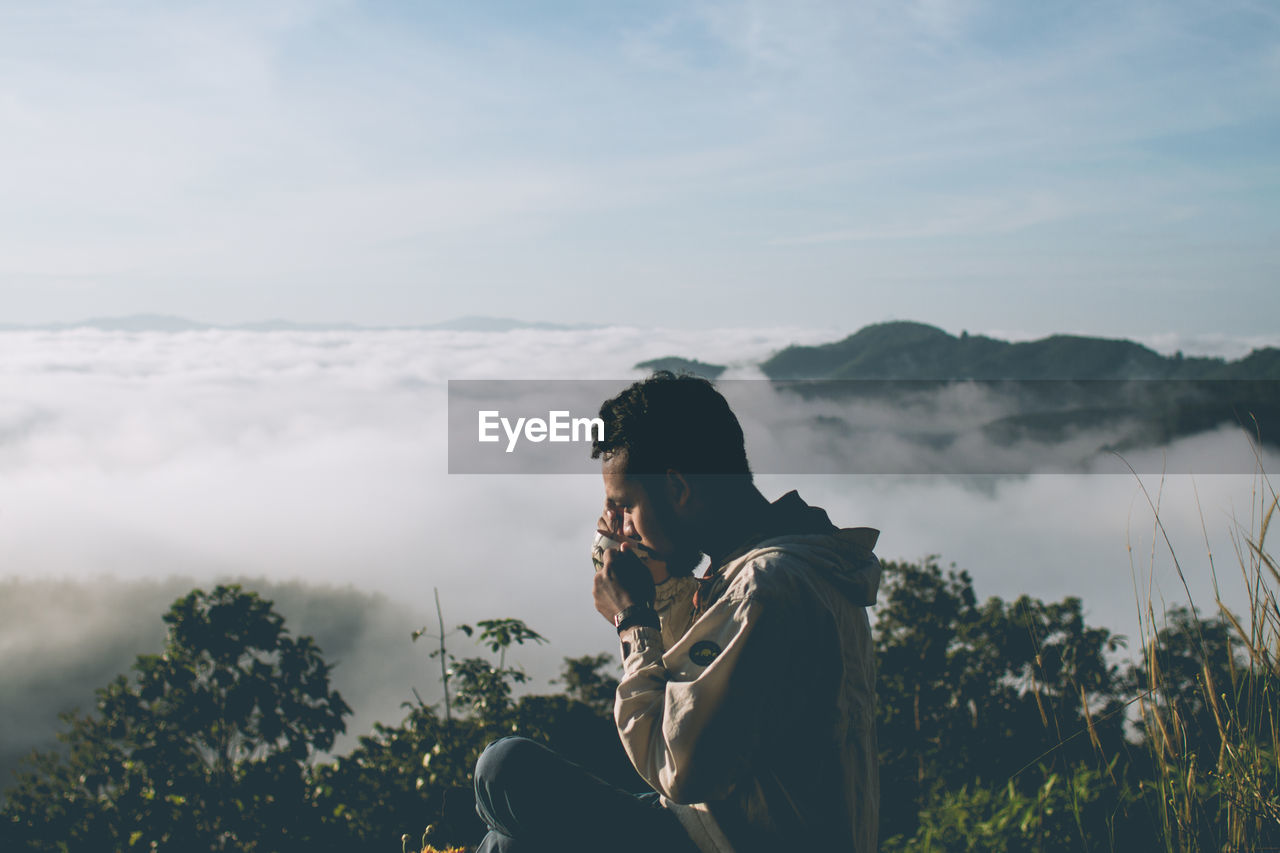 Side view of man looking at sea of mist against sky