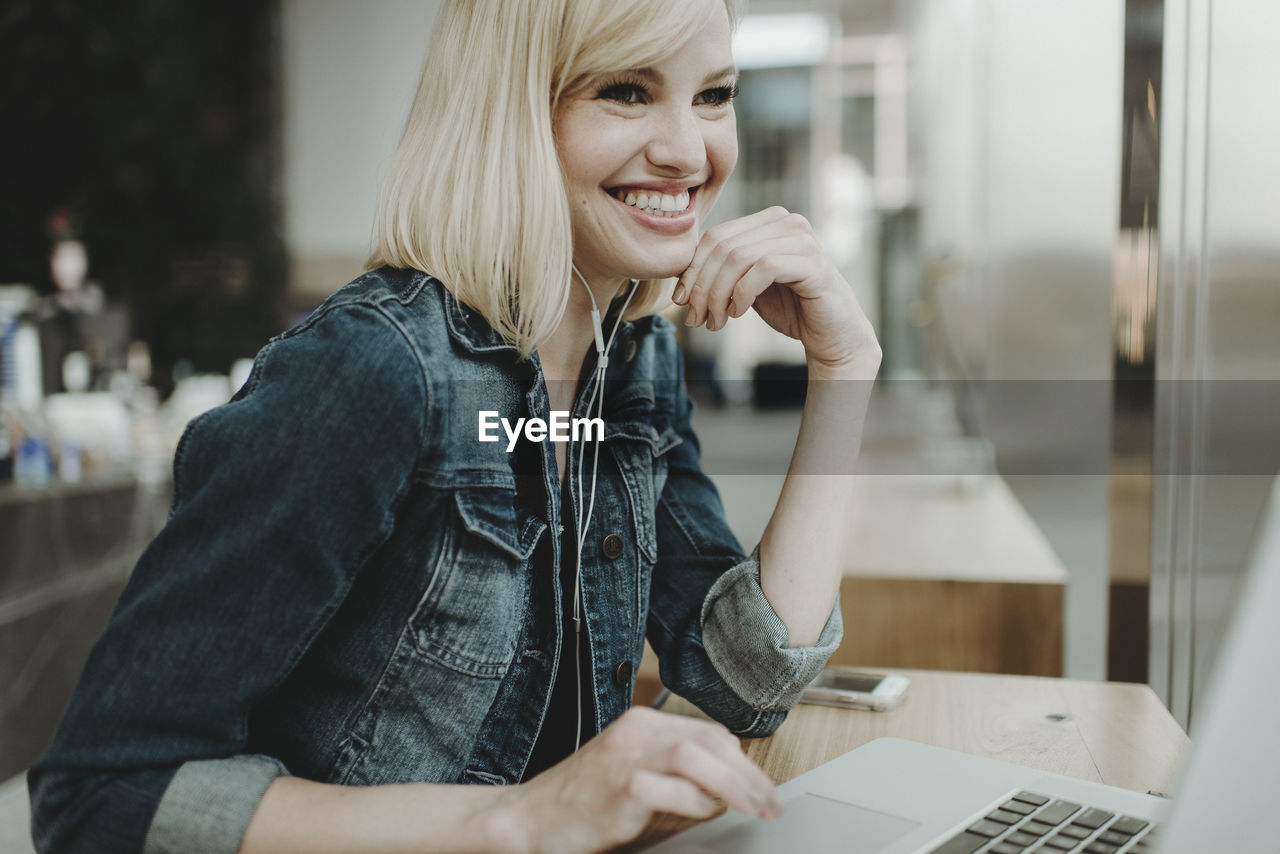 Happy woman using laptop computer while sitting by window in cafe