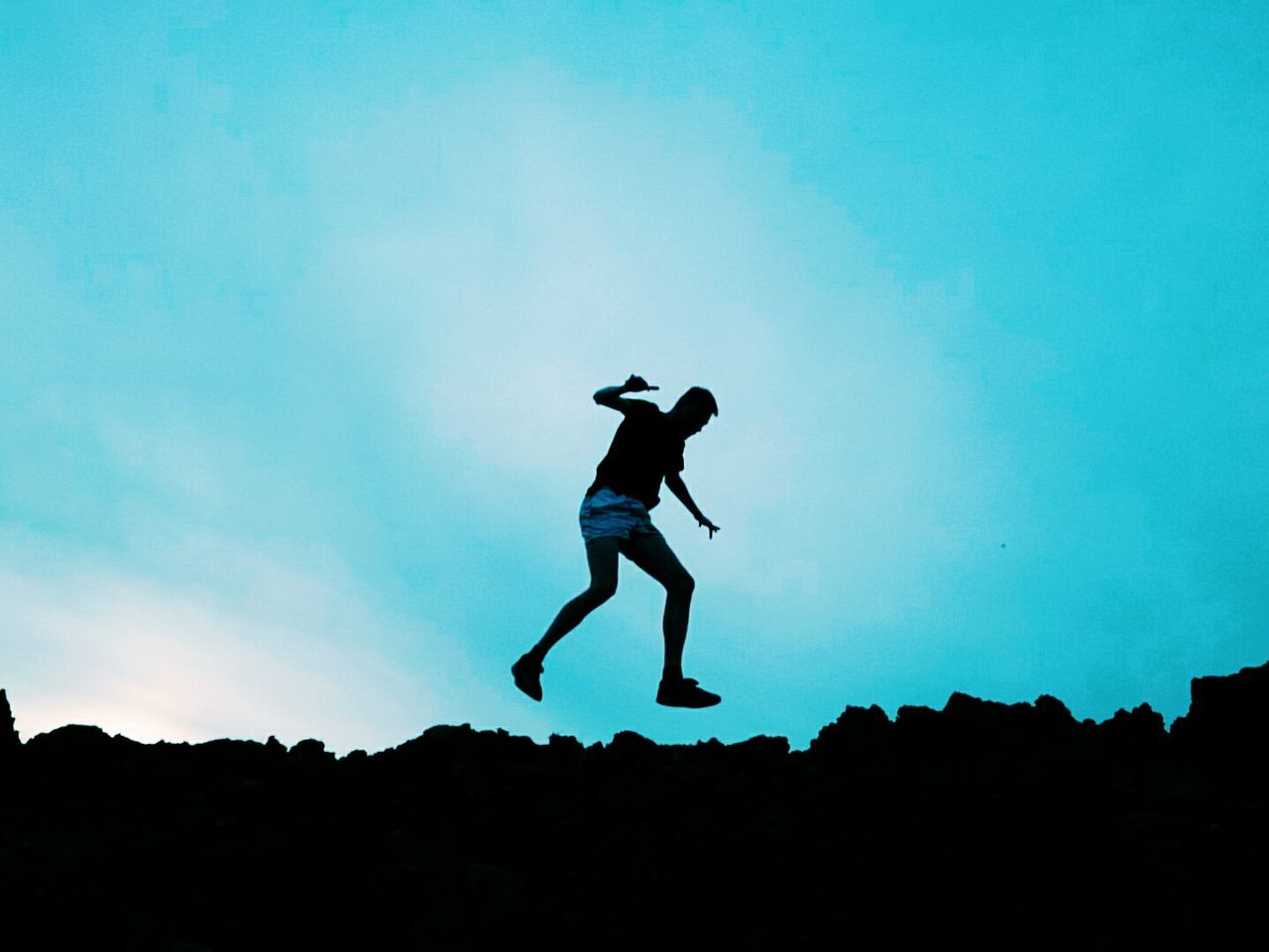 Full length of man jumping over silhouette rocks at dusk