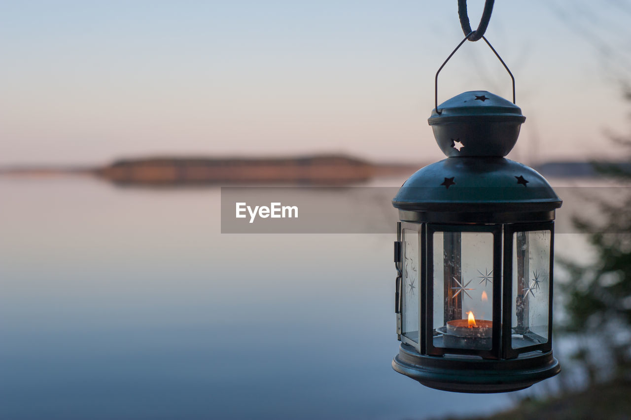 ILLUMINATED LANTERN BY LAKE AGAINST SKY