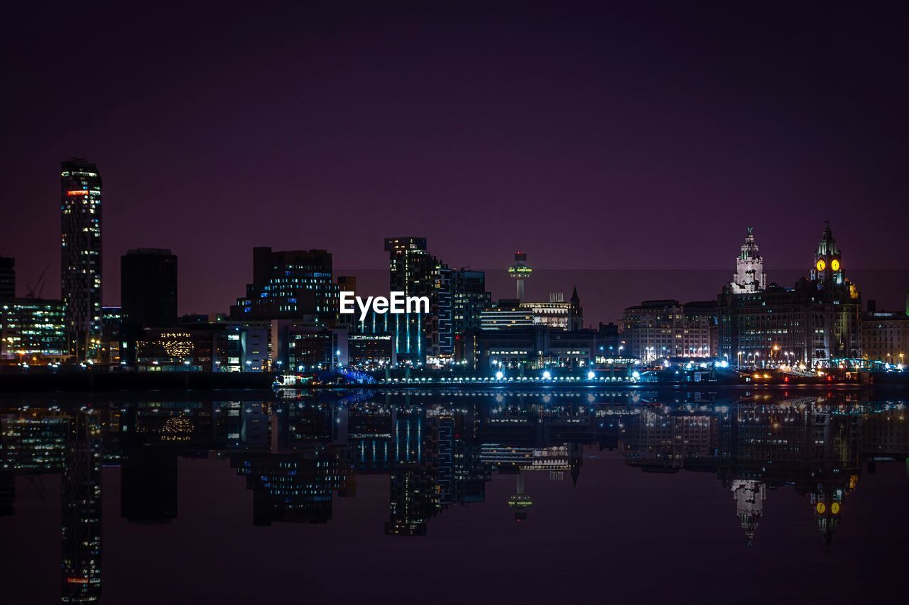 Illuminated city skyline by river against sky at night