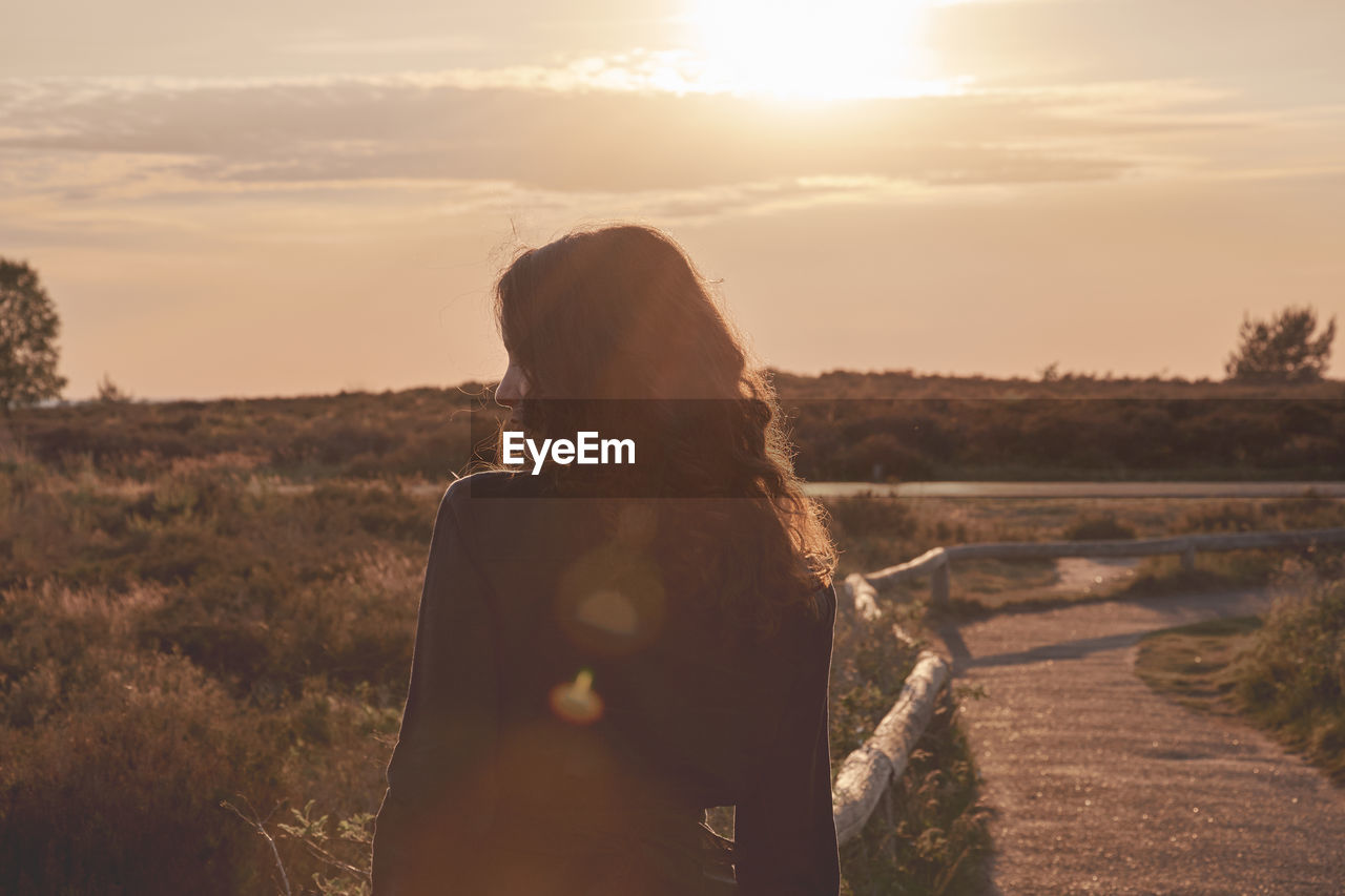 Rear view of woman standing on field against sky during sunset