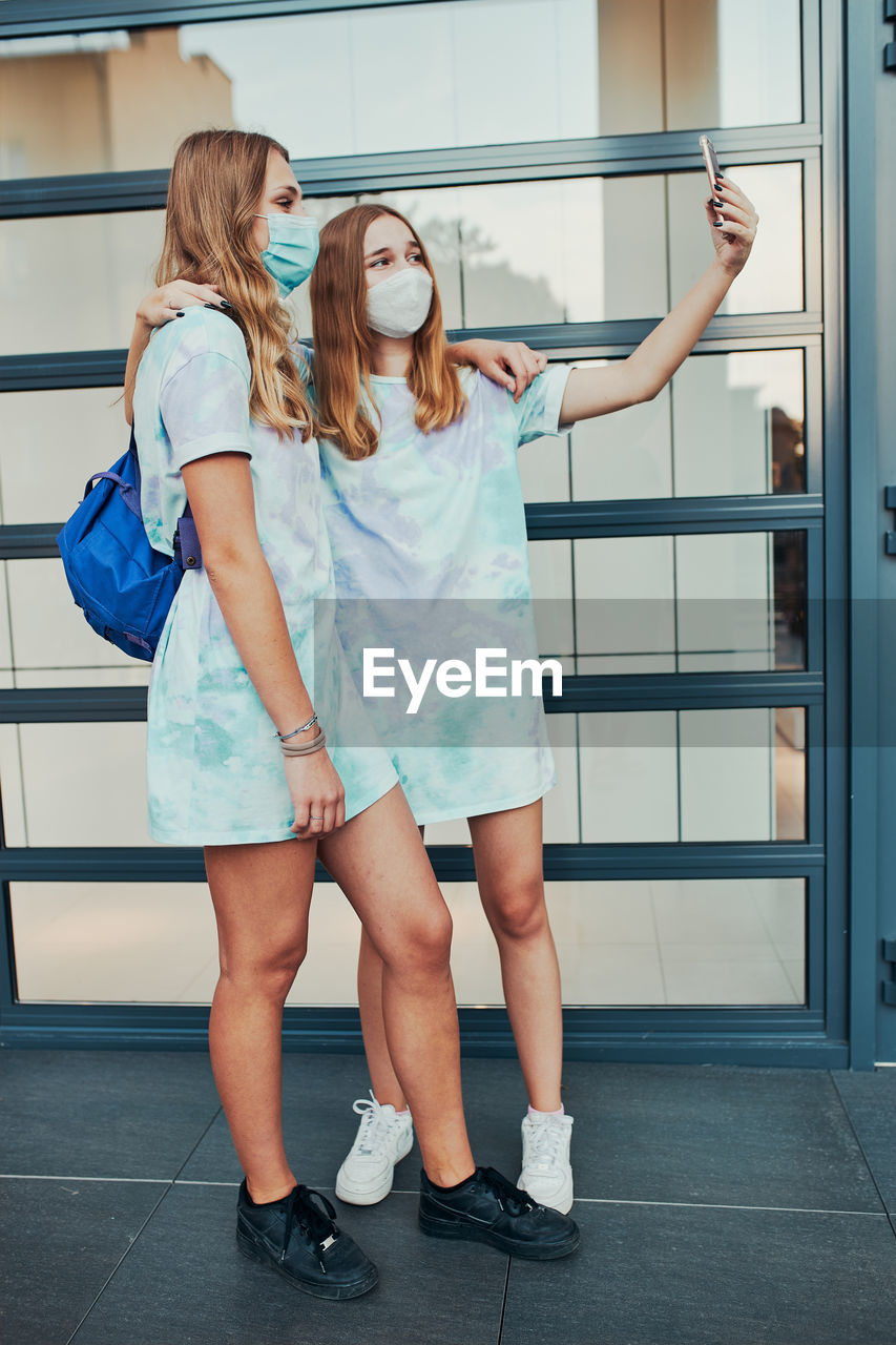 Young women girls taking selfie photos using smartphone standing at store front downtown