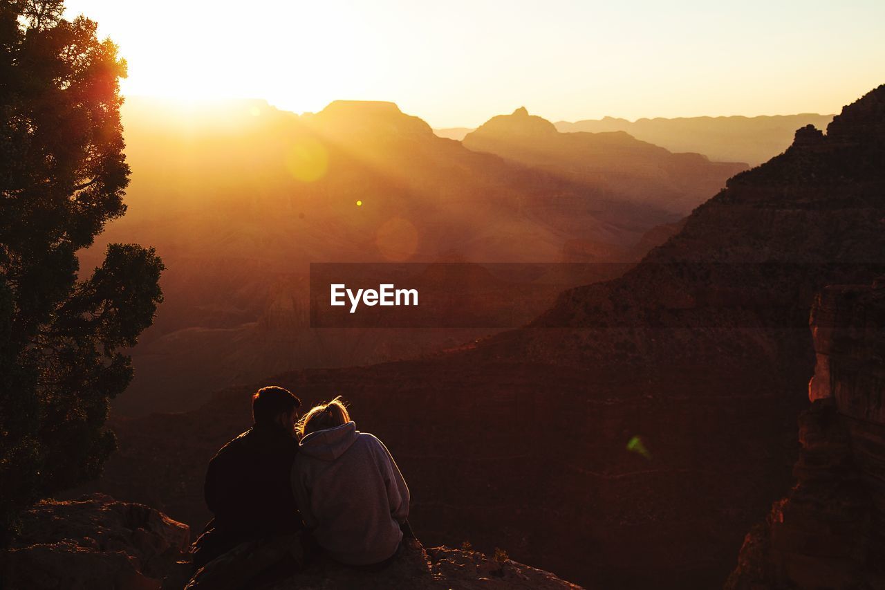 REAR VIEW OF PEOPLE ON MOUNTAIN DURING SUNSET