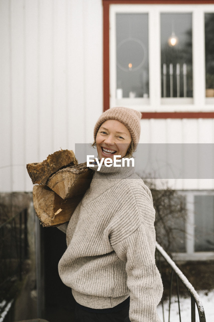 Portrait of cheerful woman carrying firewood during winter