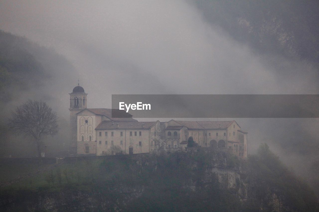 Old building and basilica by mountain during foggy weather