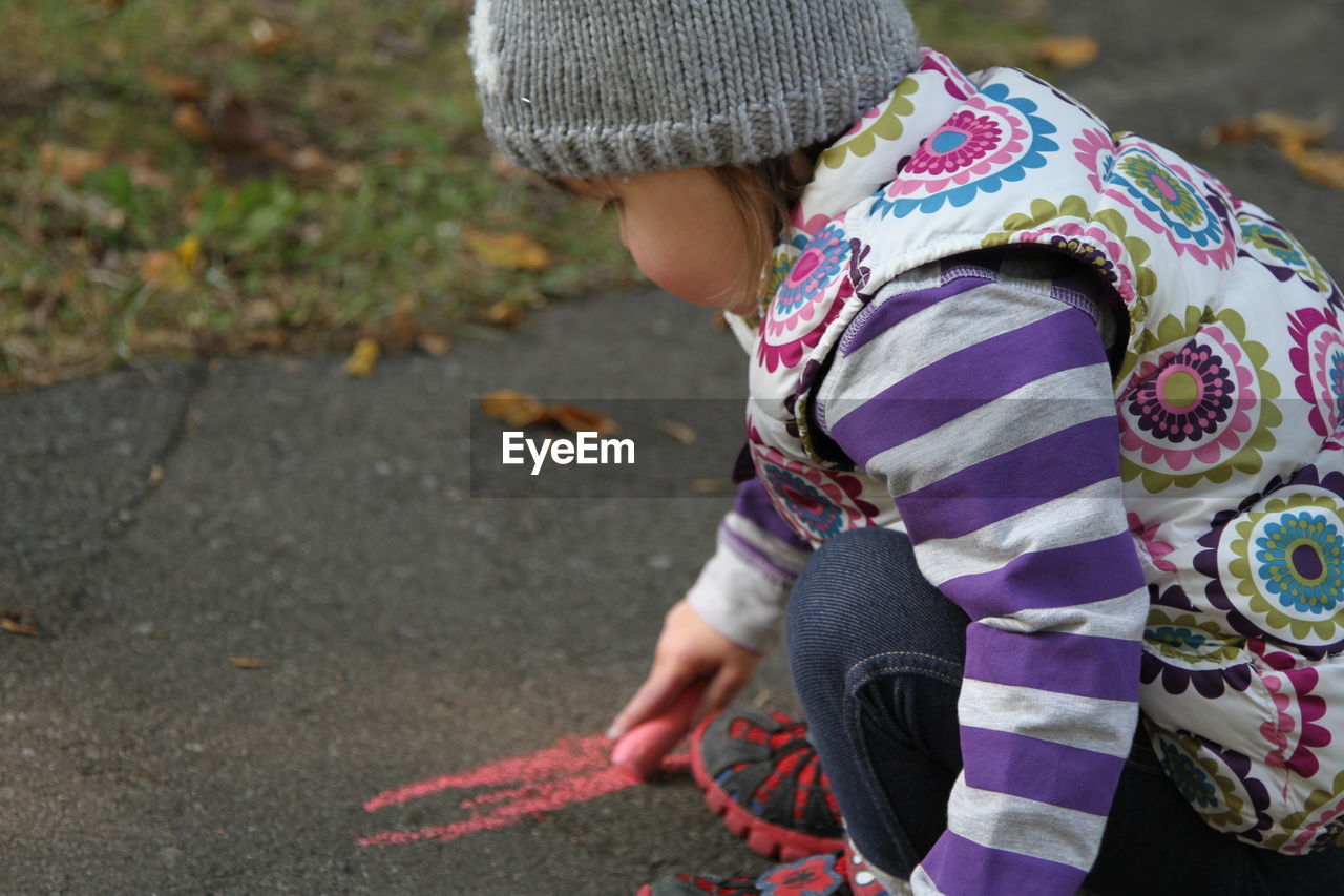 Side view of girl drawing on road with chalk during autumn