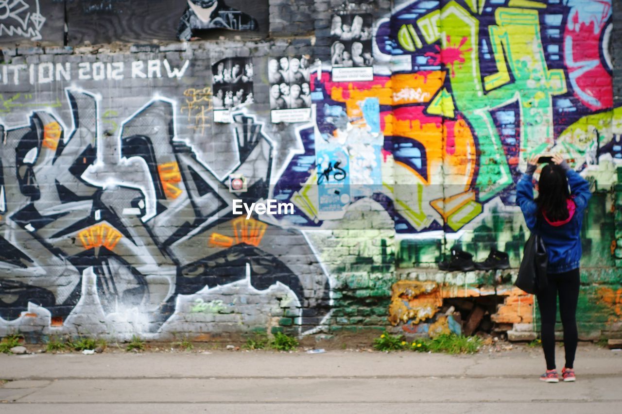 Rear view of woman photographing graffiti on wall