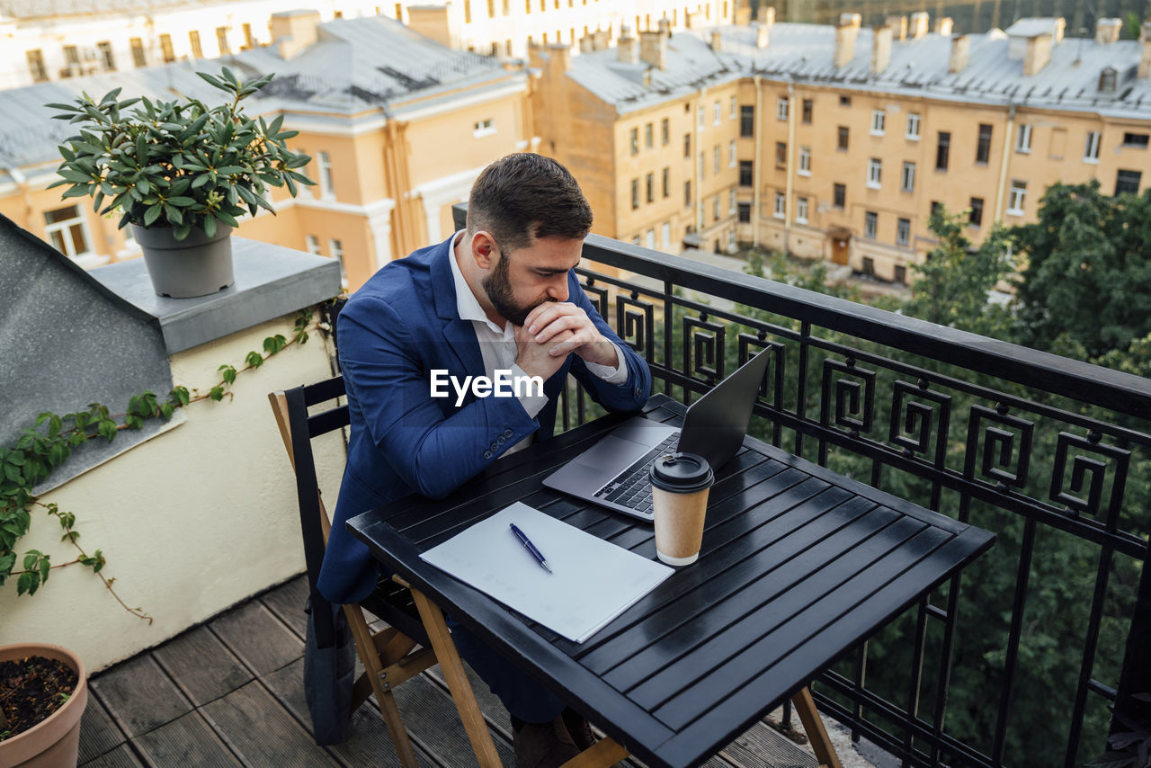 Businessman looking at laptop while sitting in office balcony