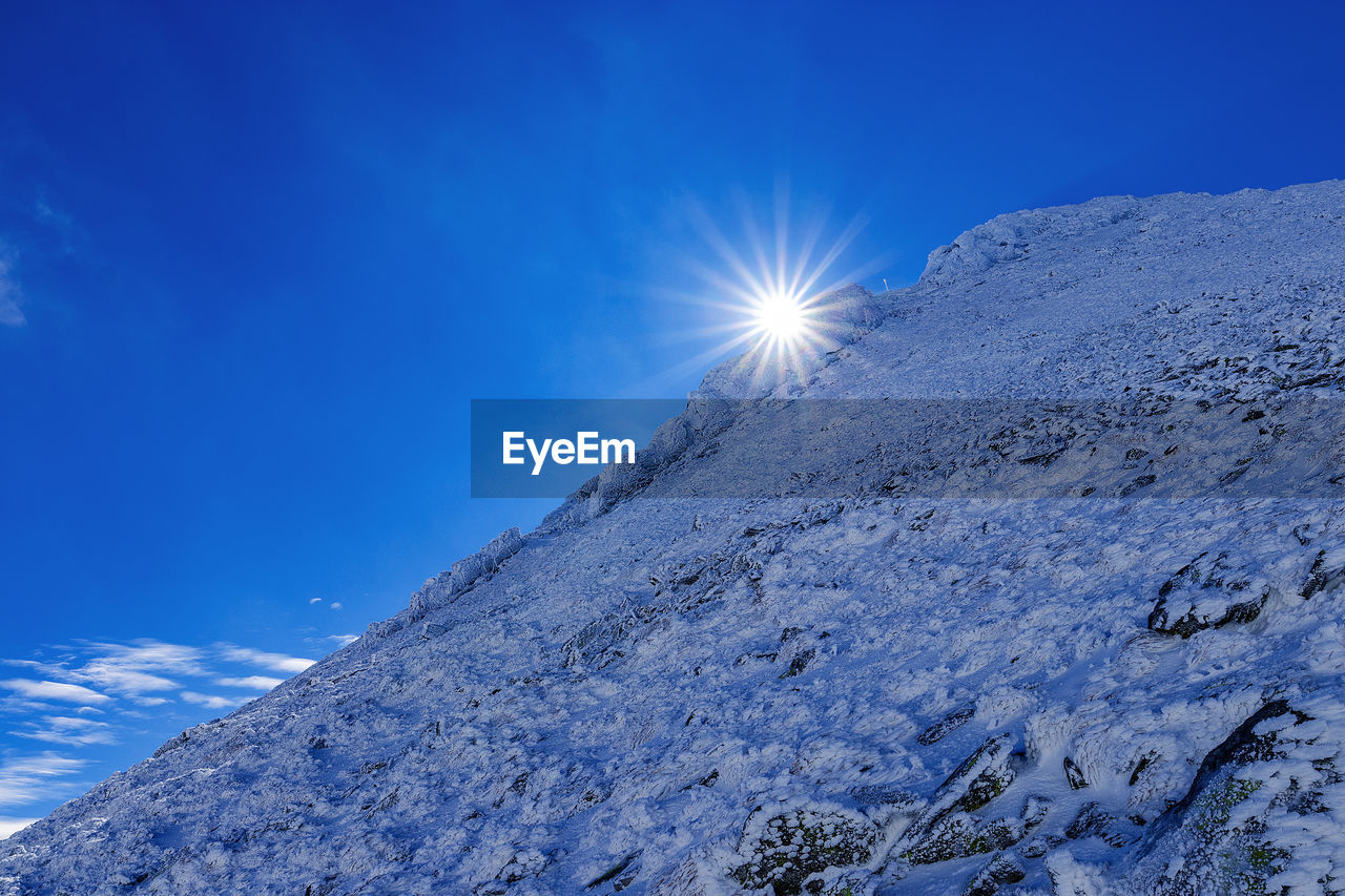 Low angle view of snowcapped mountain against blue sky