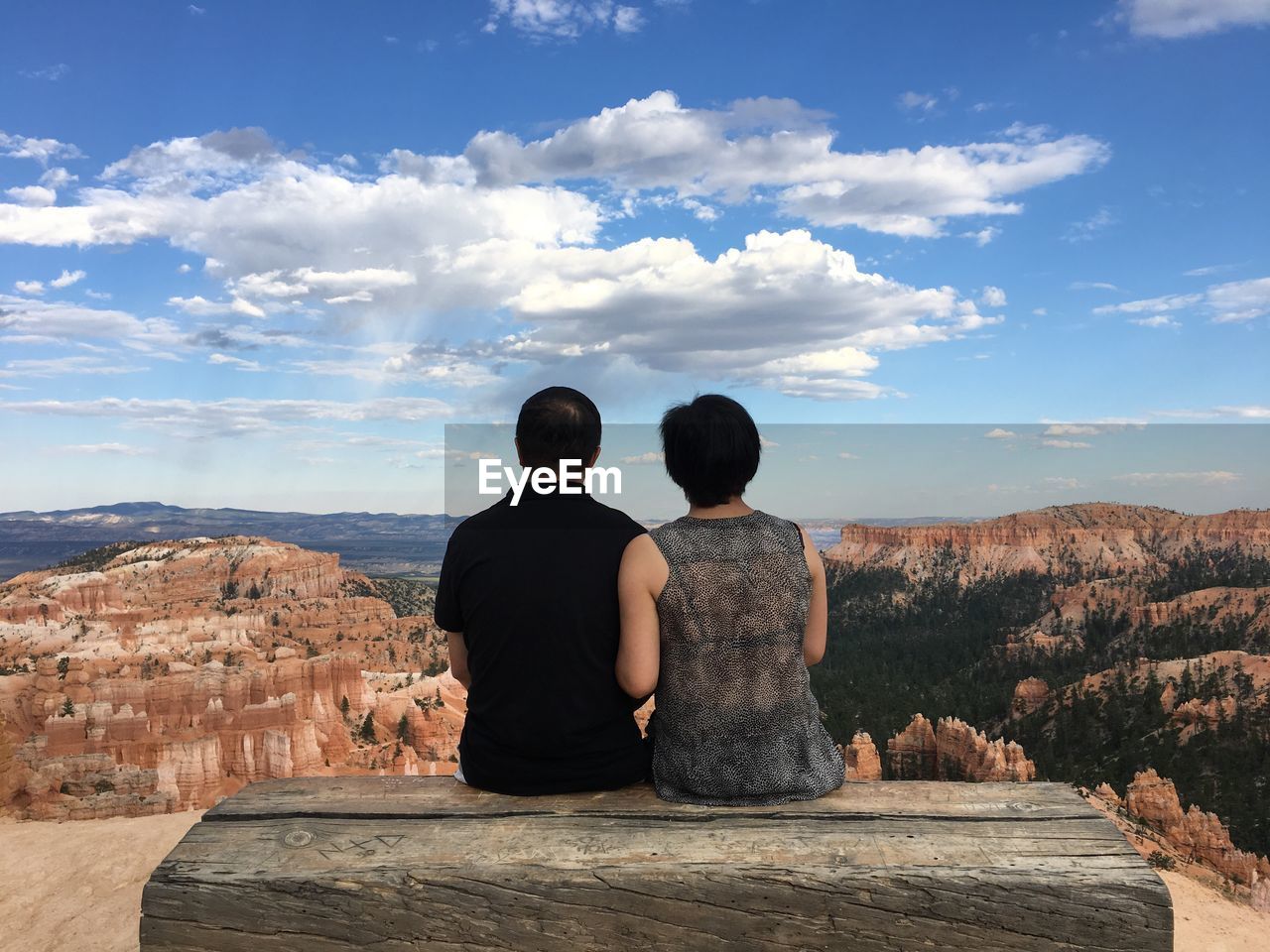 Rear view of couple sitting on rock against sky