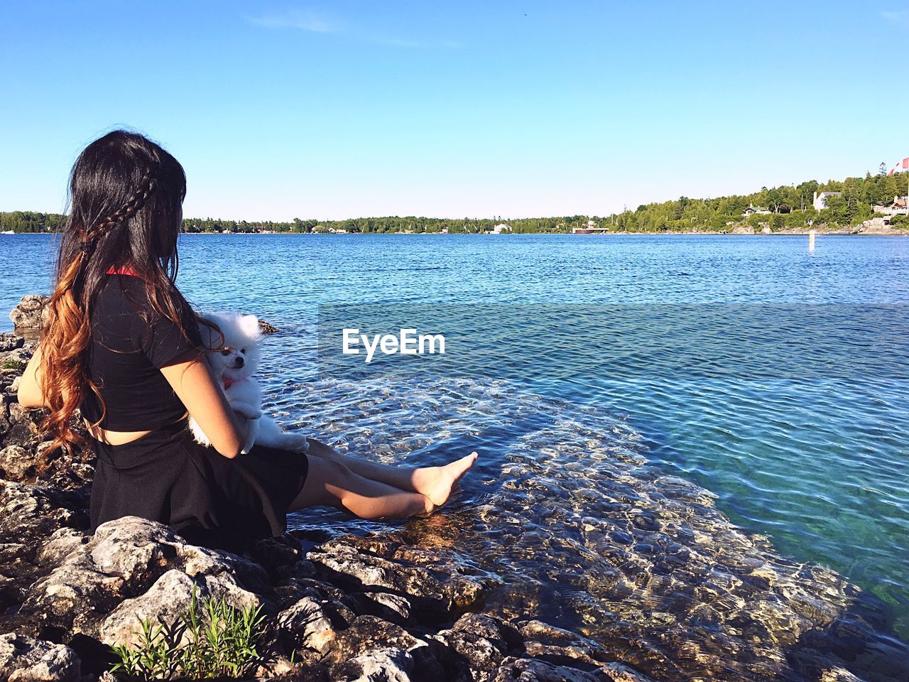 Side view of young woman sitting with pomeranian at lakeshore