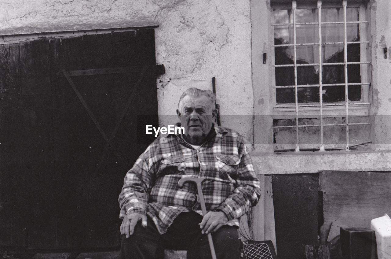 Portrait of senior man sitting against old building