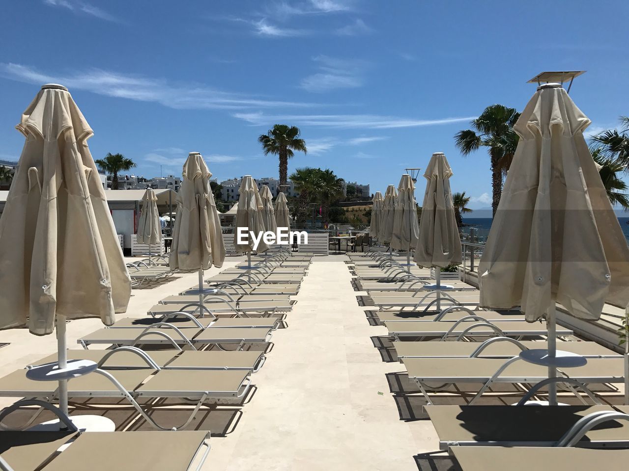 Empty lounge chairs by parasols against blue sky