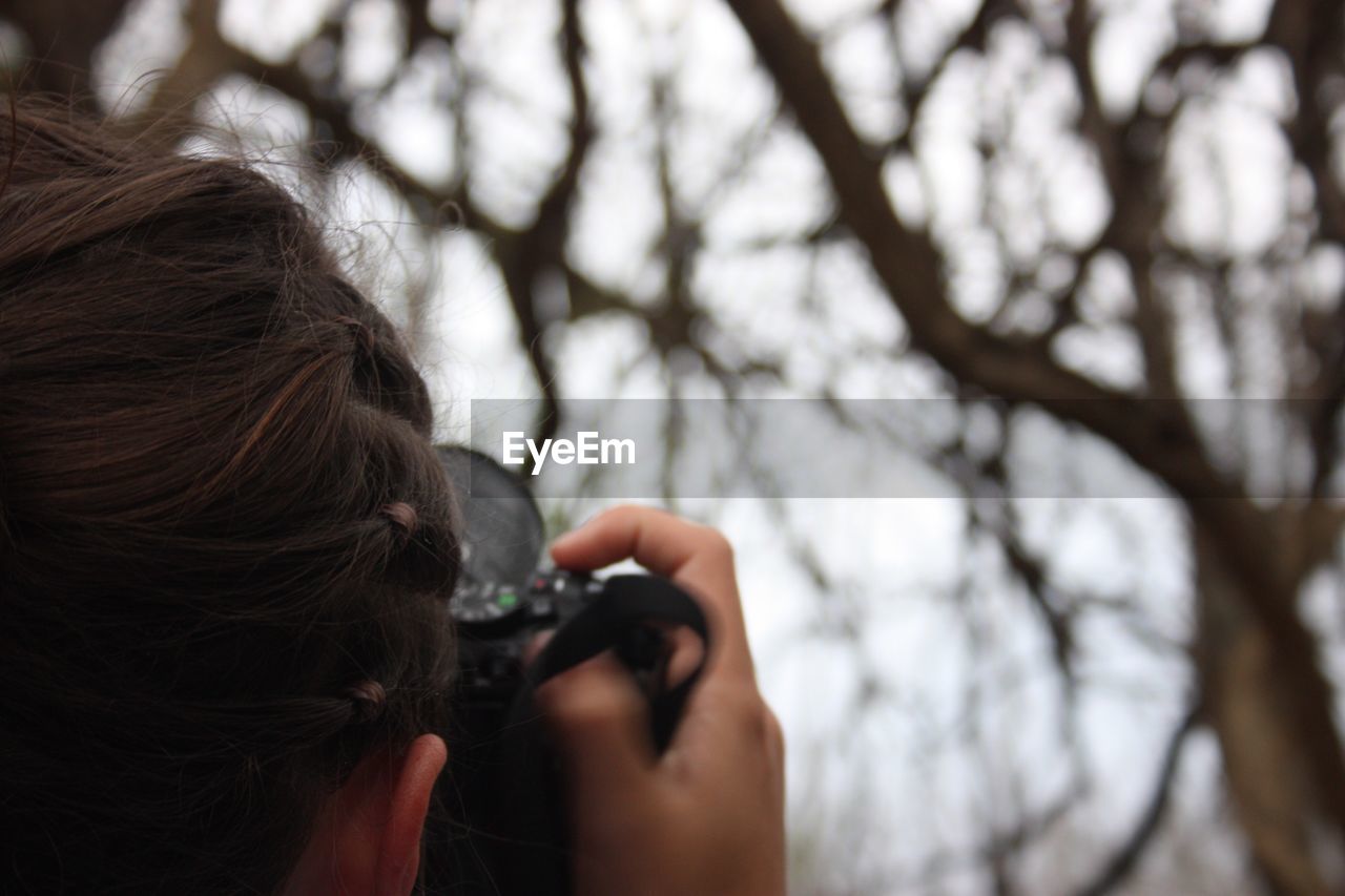 Cropped image of woman photographing against bare trees