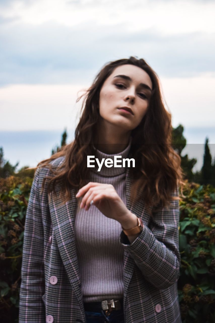 Portrait of beautiful young woman standing against sky