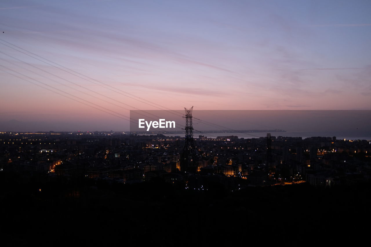 HIGH ANGLE VIEW OF ILLUMINATED CITY BUILDINGS AGAINST SKY AT SUNSET