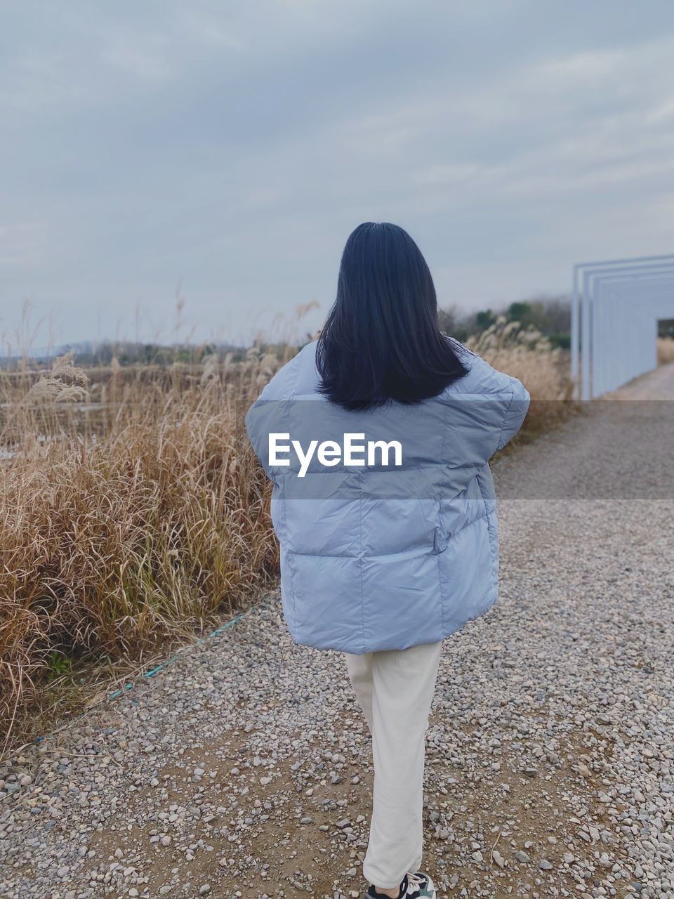 rear view, one person, blue, women, sky, nature, standing, full length, adult, land, casual clothing, cloud, leisure activity, day, lifestyles, long hair, hairstyle, spring, young adult, sand, plant, female, outdoors, field, beach, tranquility, beauty in nature, walking, clothing, white, non-urban scene, person, landscape