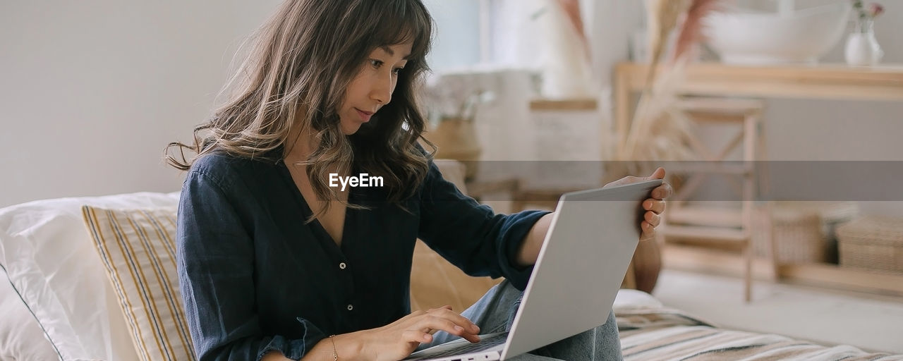 Young woman using laptop while sitting on bed at home