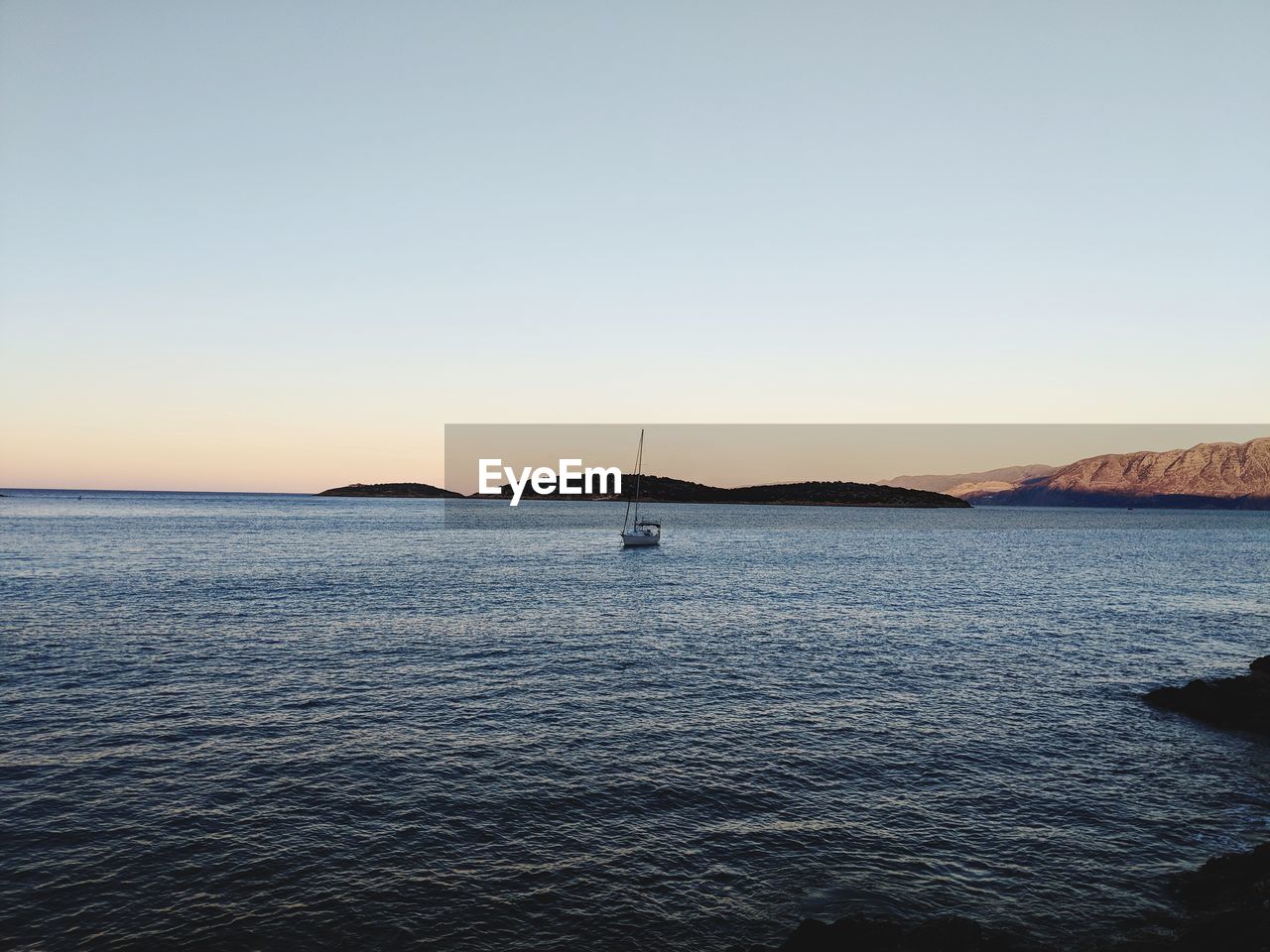 Sailboat in sea against clear sky during sunset