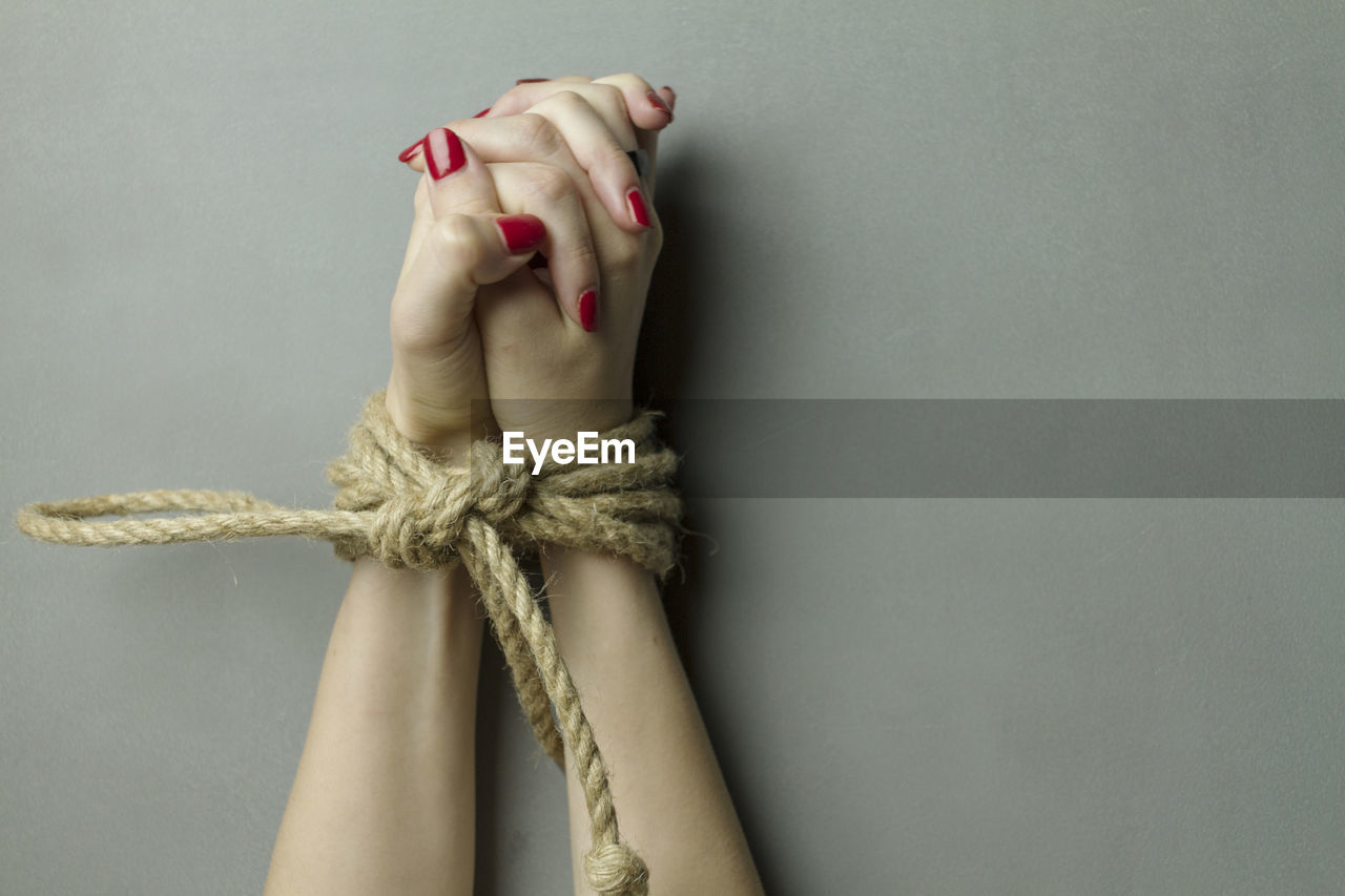 Close-up of hands tied with rope on gray background