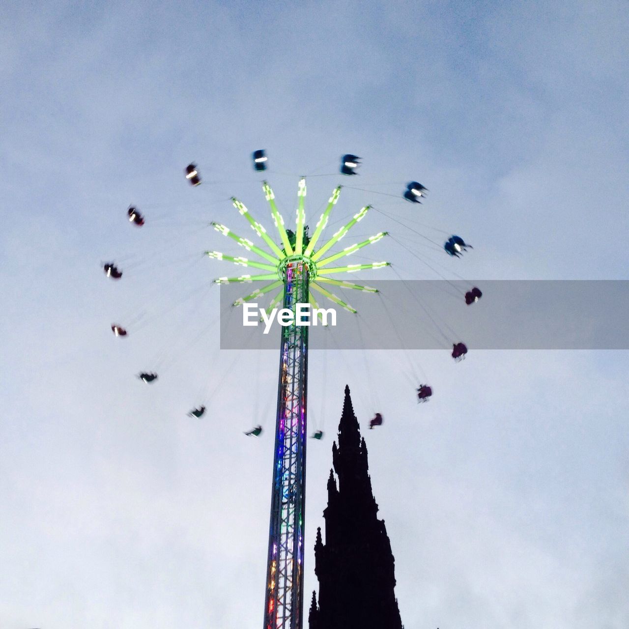 Low angle view of illuminated chain swing ride by silhouetted castle