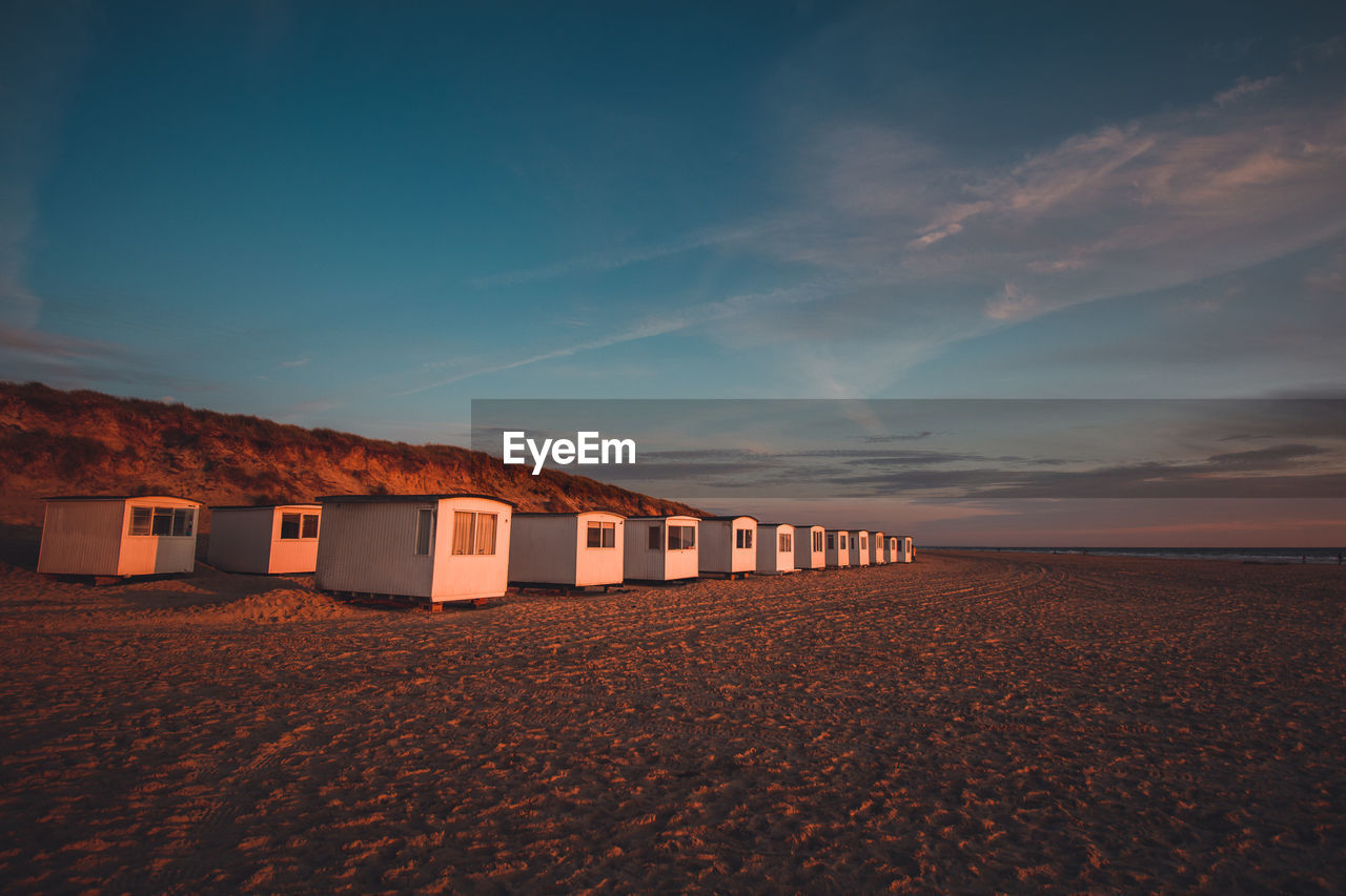 Huts at beach against blue sky during sunset