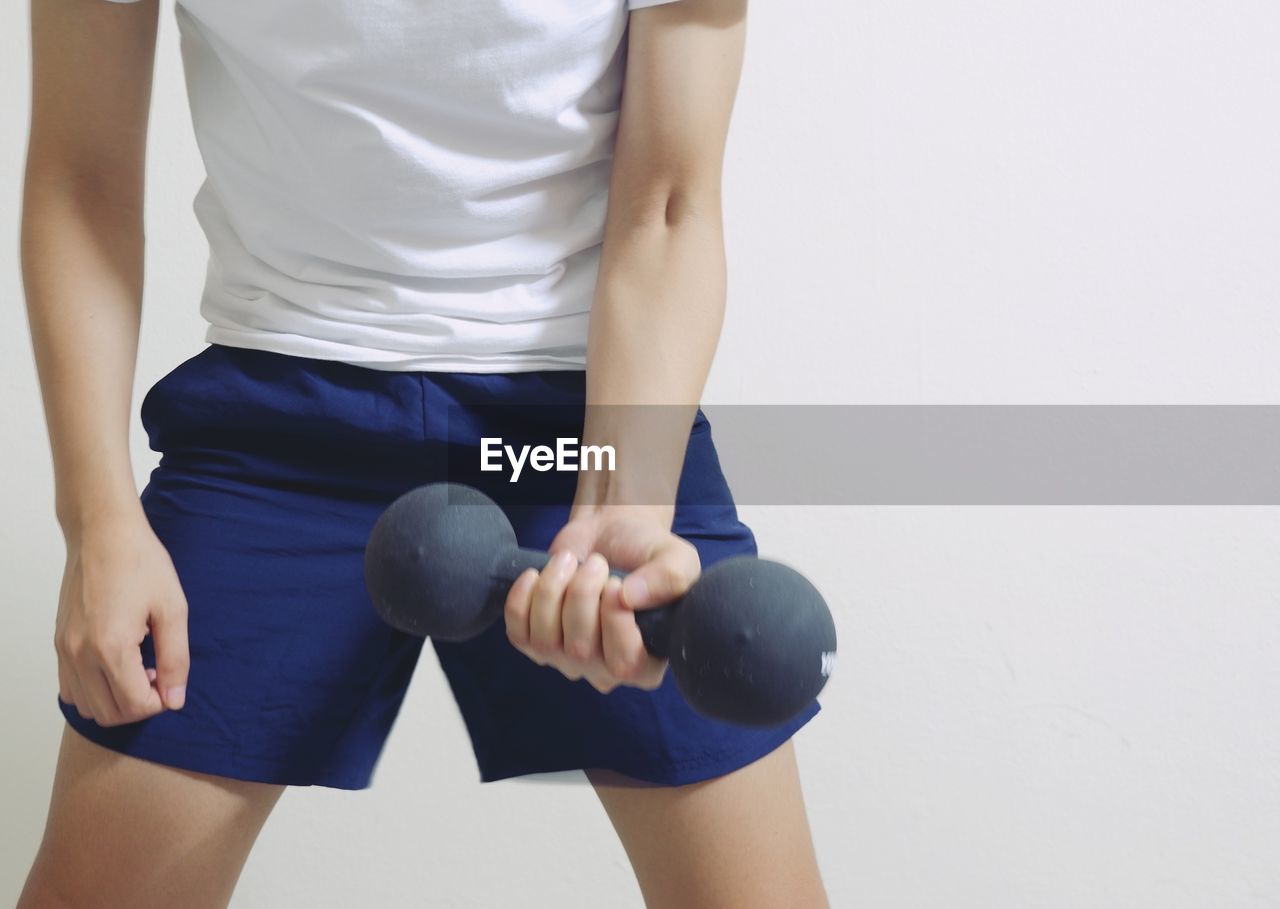 Midsection of man holding dumbbell while standing against wall