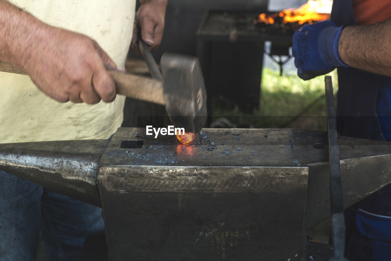 Midsection of manual worker hitting on molten metal in industry