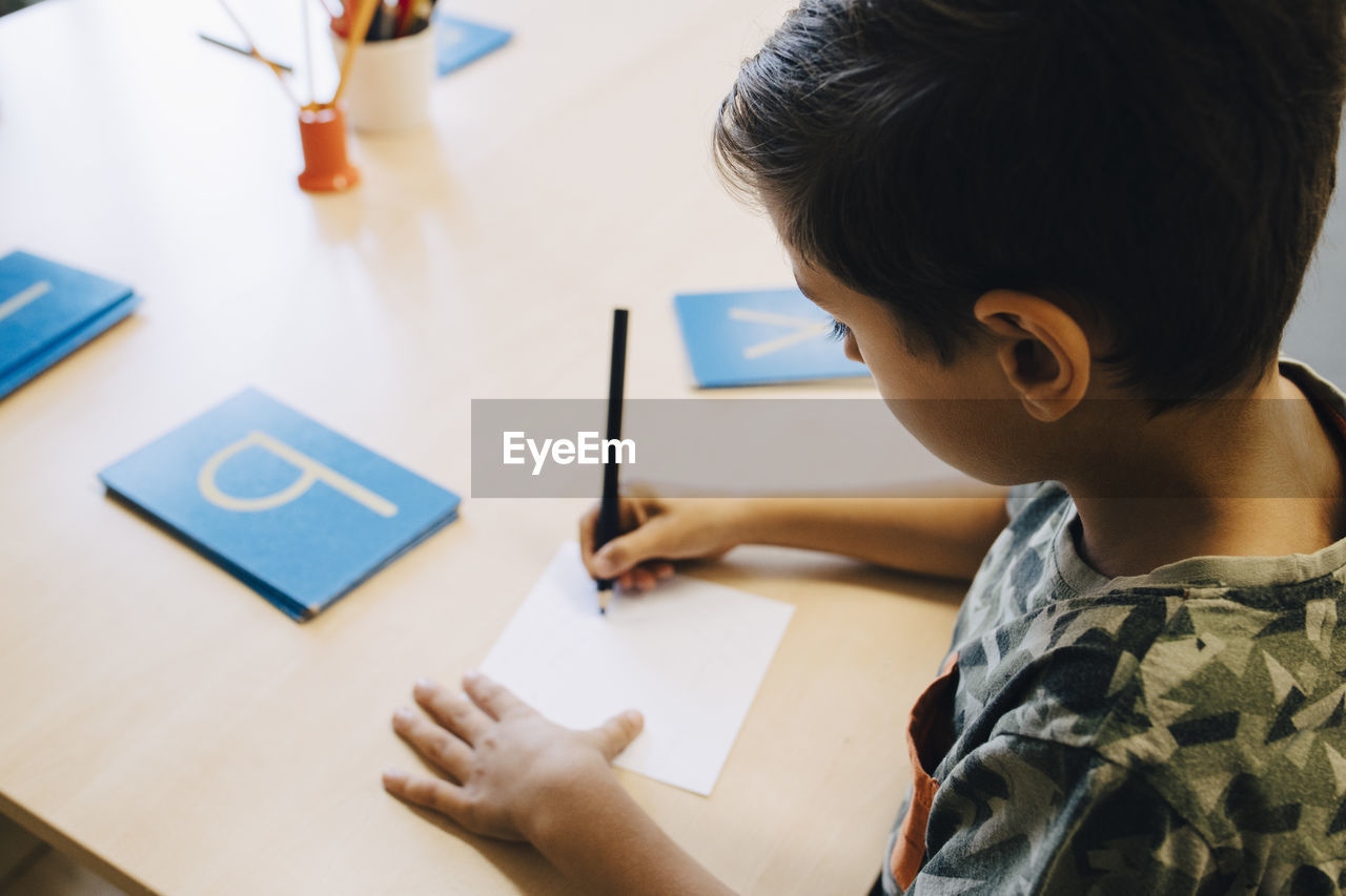 High angle view of schoolboy practicing alphabets at table in classroom