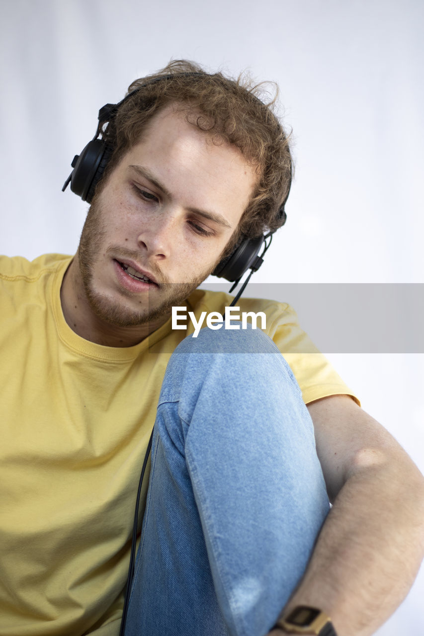 Portrait of young man sitting against white background in a yellow shirt doing music