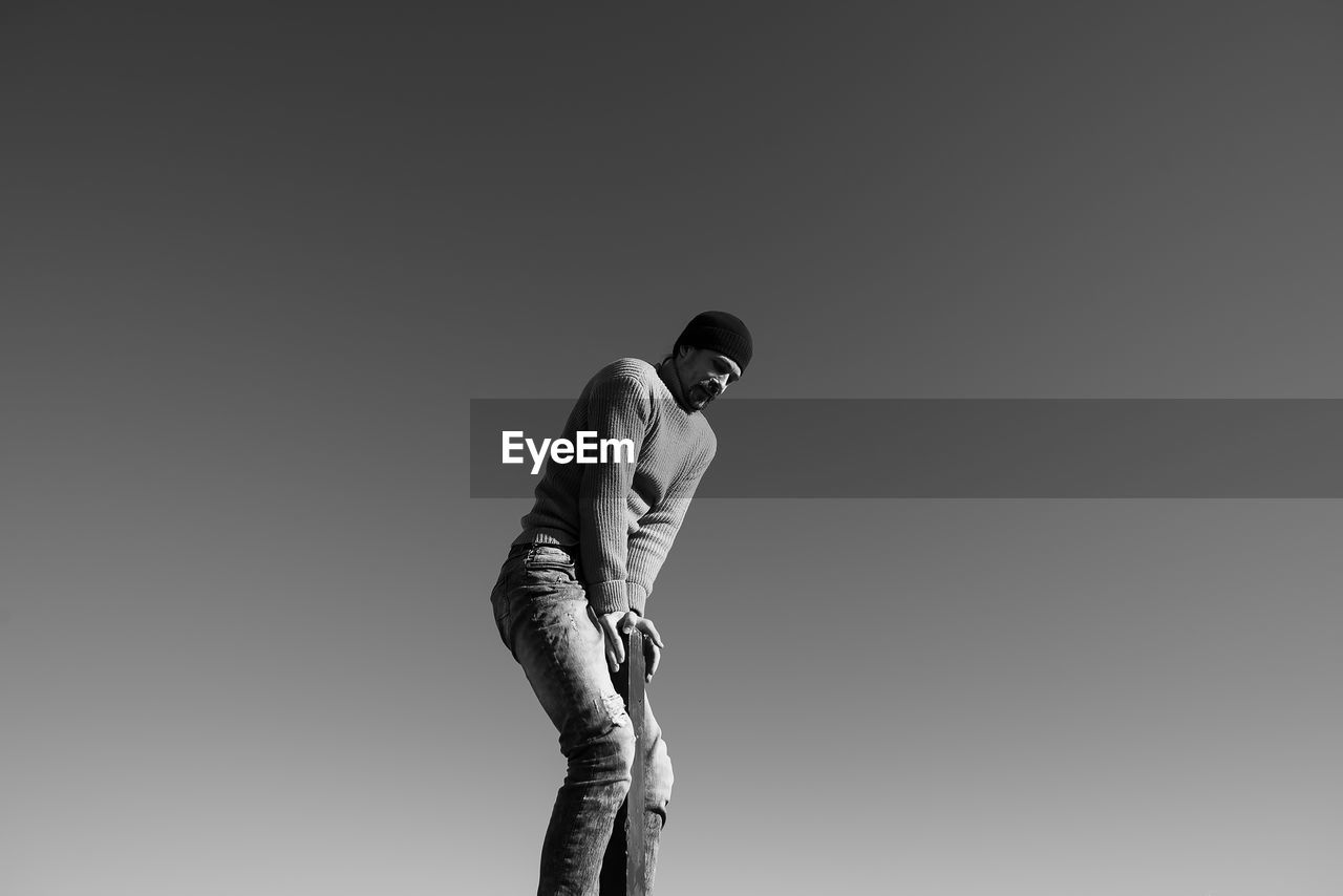 Low angle view of man balancing on pole against clear sky