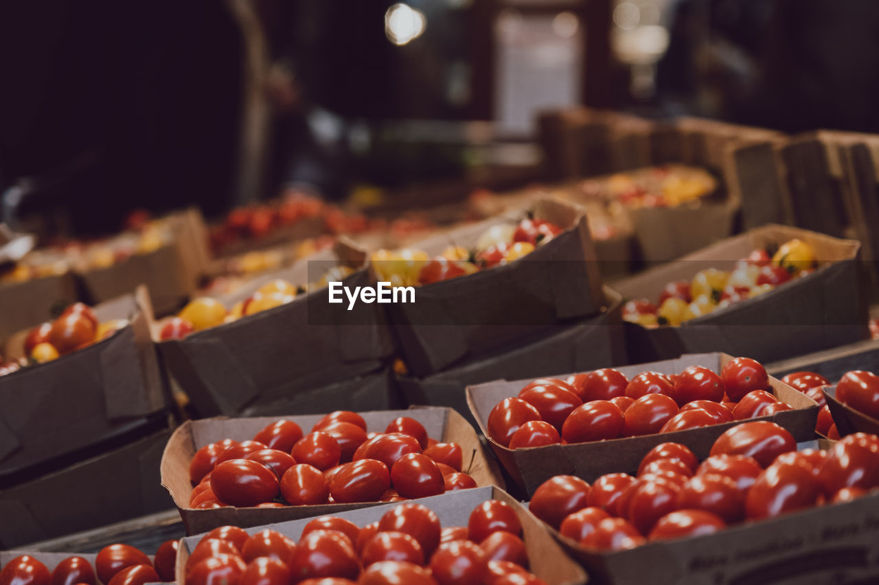 Various tomatoes in paper punnets for sale at market stall, selective focus, bokeh.