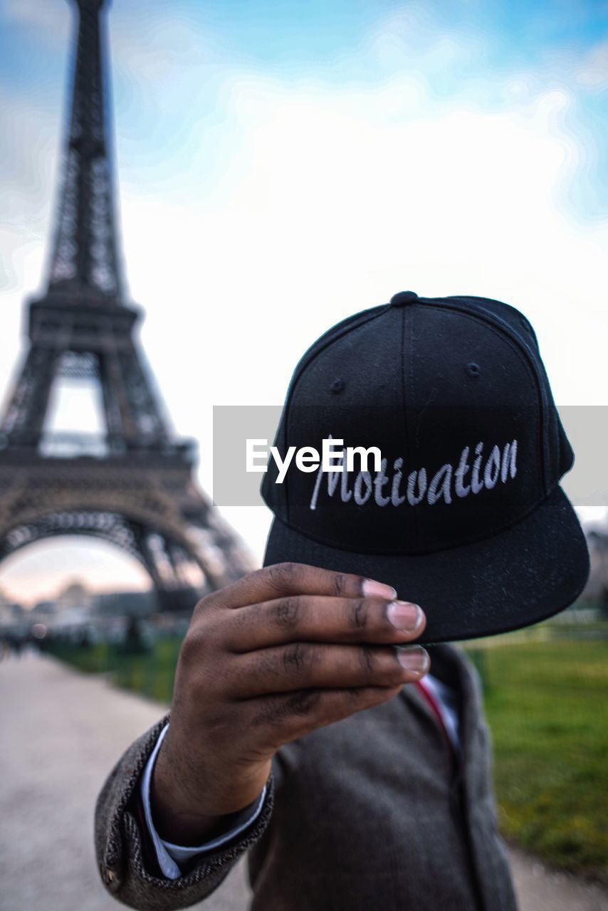 Man holding cap with text while standing against eiffel tower