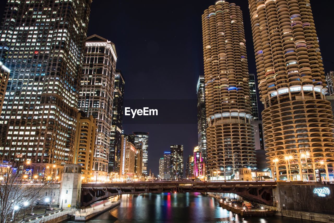 Illuminated buildings by river against sky at night