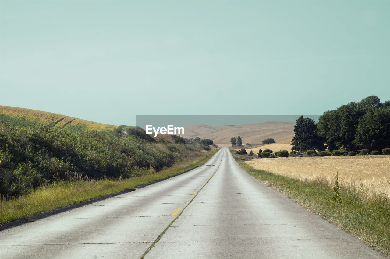 Road amidst field against clear sky