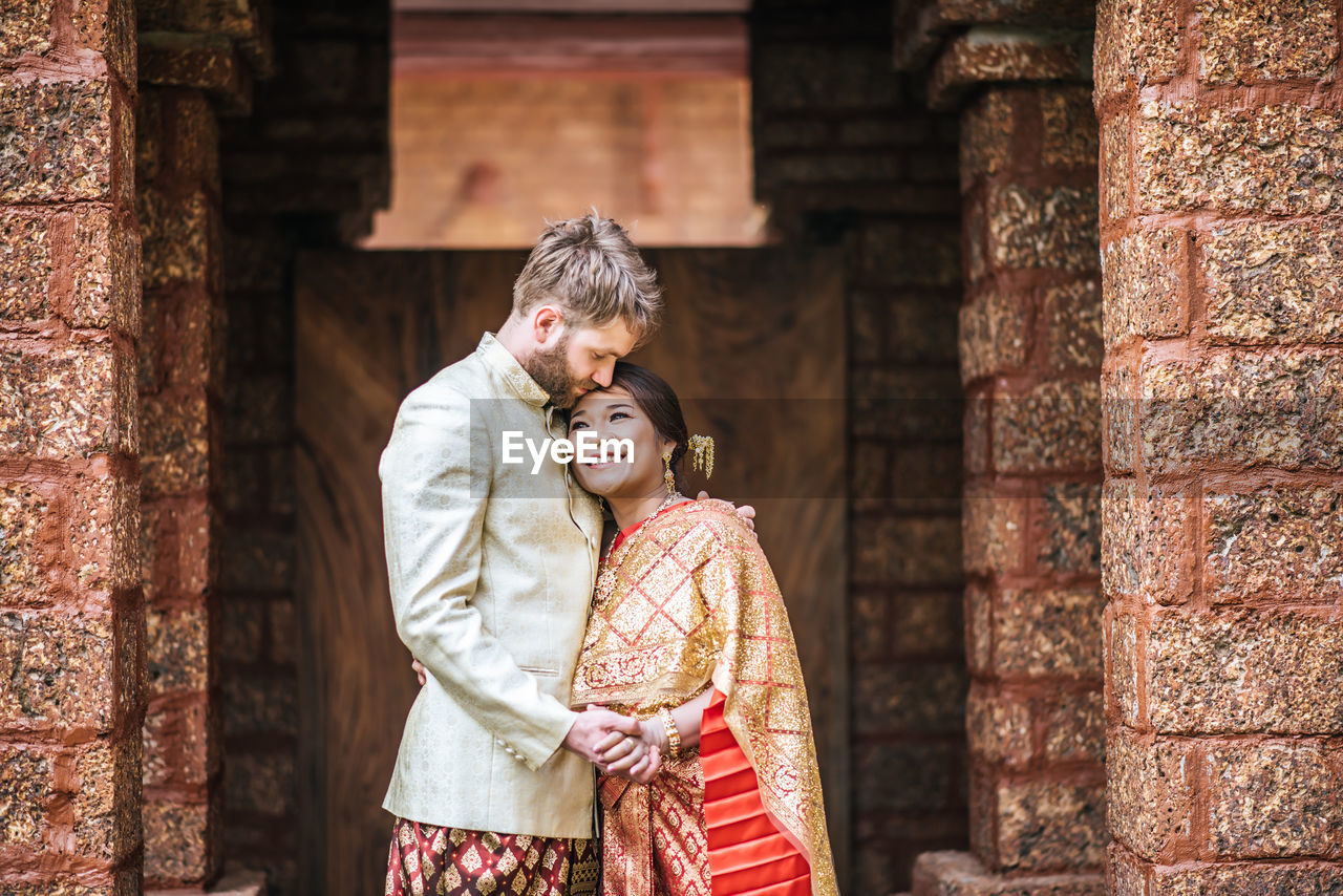 Couple holding hands while standing against building