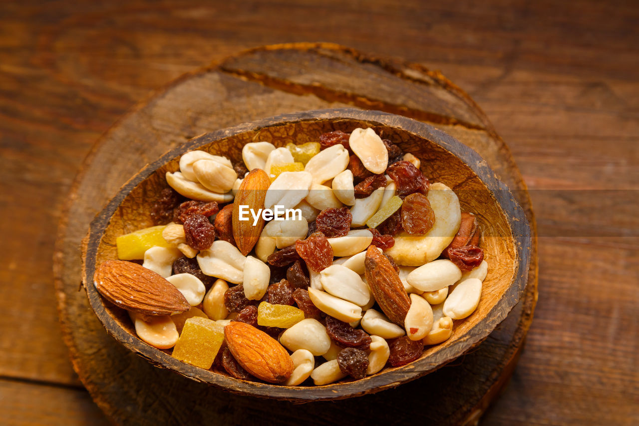 A mixture of dried fruits and nuts in a coconut shell plate on a wooden table.