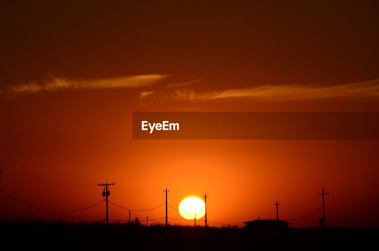 Telephone poles on field against orange sky